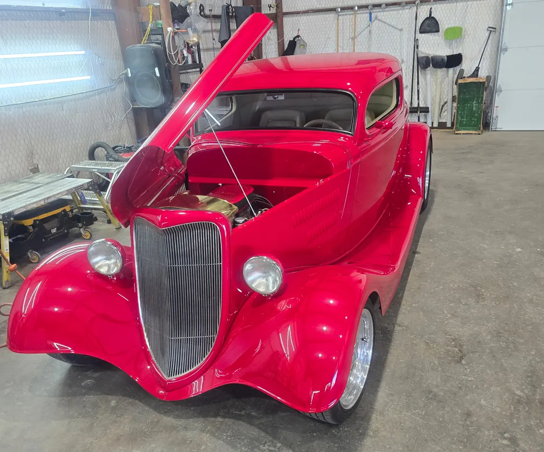 Red 1934 Ford three window coupe hot rod, hood up, in the shop bay