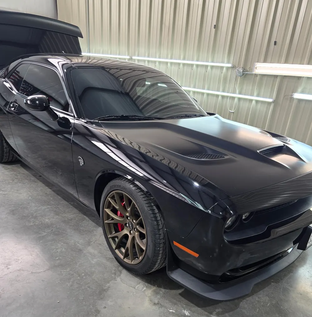 Black Dodge Challenger Hellcat with dark tinted glass, in the shop bay