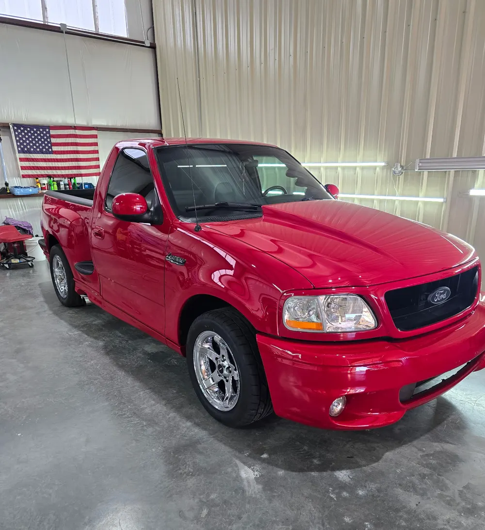 Red Ford SVT Lightning on chrome wheels, tinted glass, in the shop bay