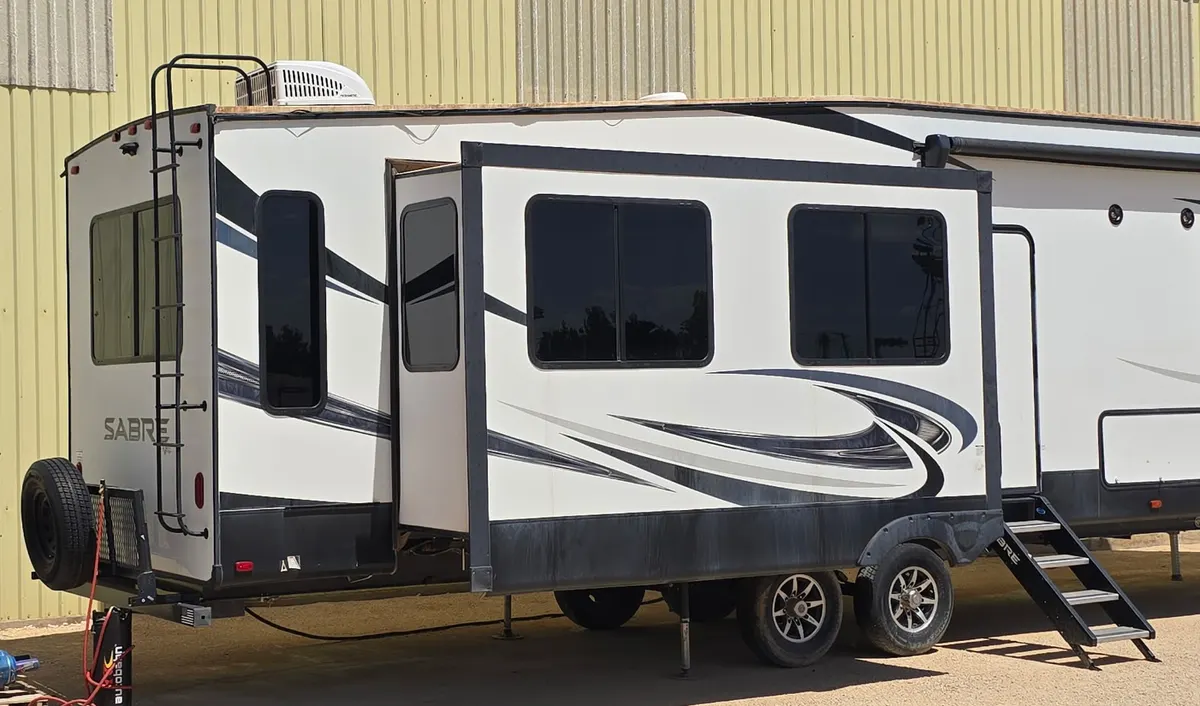 White Forest River Sabre fifth wheel RV in profile, slide out extended, tinted windows